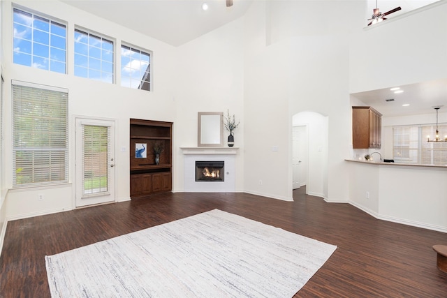 unfurnished living room with a lit fireplace, a towering ceiling, arched walkways, baseboards, and dark wood-type flooring