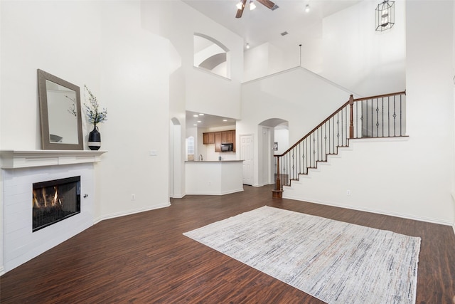 unfurnished living room featuring arched walkways, dark wood finished floors, ceiling fan, and a fireplace