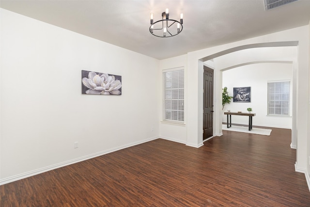 spare room with visible vents, arched walkways, dark wood finished floors, baseboards, and a chandelier