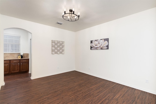 empty room with a notable chandelier, arched walkways, baseboards, visible vents, and dark wood-style floors