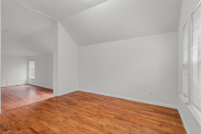 additional living space with baseboards, vaulted ceiling, and light wood-type flooring