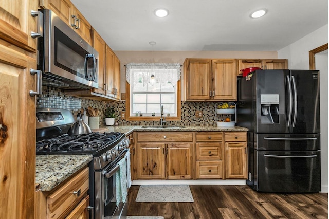 kitchen with light stone countertops, appliances with stainless steel finishes, a sink, brown cabinetry, and dark wood-type flooring