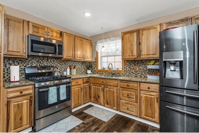 kitchen featuring decorative backsplash, light stone countertops, dark wood finished floors, a sink, and stainless steel appliances