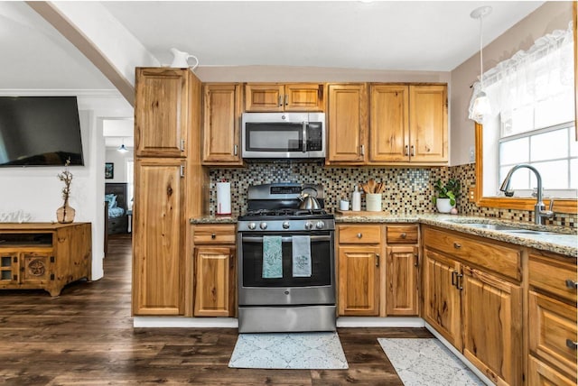 kitchen with dark wood-style flooring, light stone countertops, appliances with stainless steel finishes, a sink, and tasteful backsplash