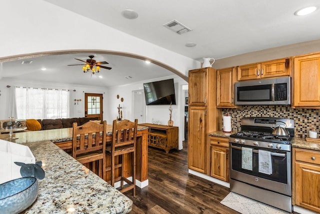kitchen featuring ceiling fan, appliances with stainless steel finishes, light stone countertops, arched walkways, and visible vents