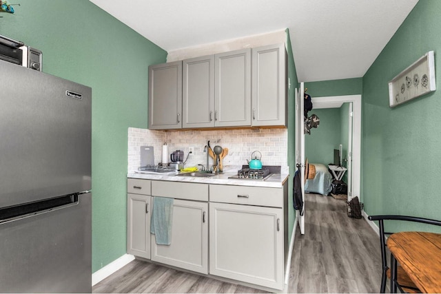 kitchen with backsplash, a sink, light countertops, light wood-style floors, and stainless steel appliances