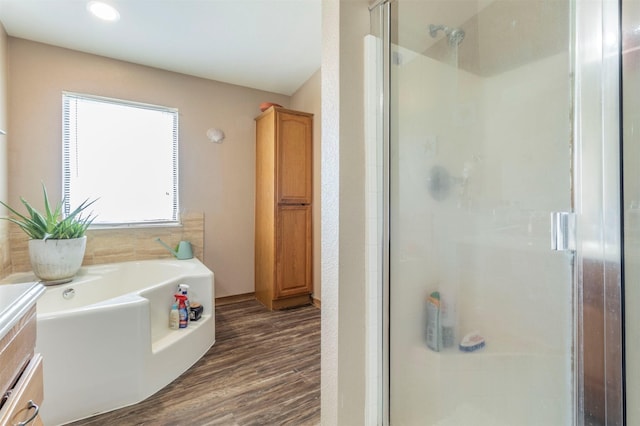 full bathroom with wood finished floors, a bath, and a stall shower