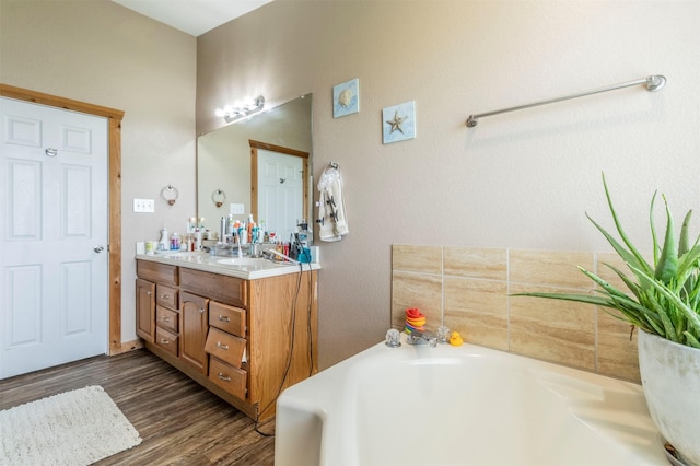 full bath featuring wood finished floors, a garden tub, and vanity