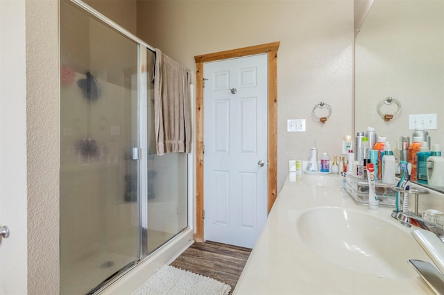 full bathroom featuring a sink, double vanity, a shower stall, and wood finished floors