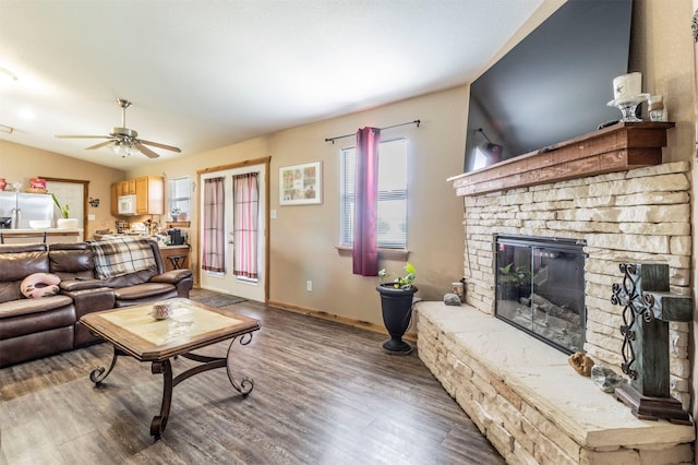 living area with vaulted ceiling, a fireplace, a ceiling fan, and wood finished floors