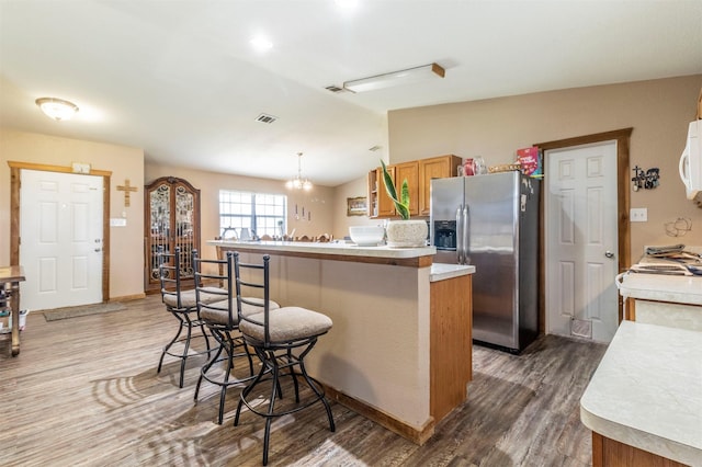 kitchen featuring visible vents, wood finished floors, a breakfast bar, light countertops, and stainless steel fridge with ice dispenser