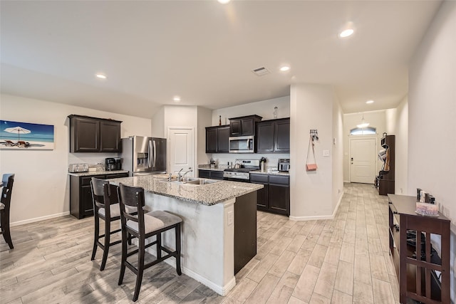kitchen with an island with sink, light wood-style flooring, appliances with stainless steel finishes, and light stone countertops