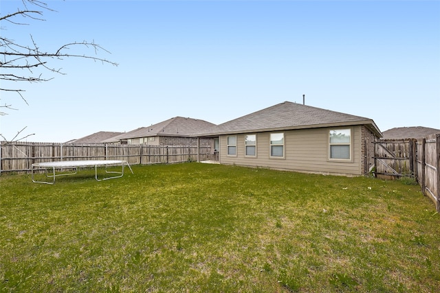 back of house featuring a lawn, a fenced backyard, and a trampoline