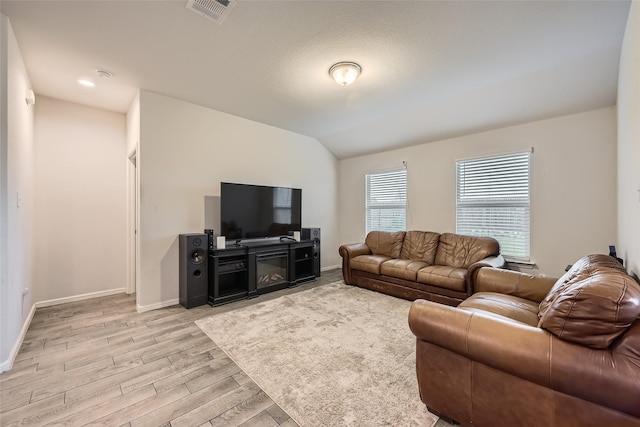 living area with visible vents, light wood-style floors, baseboards, and vaulted ceiling