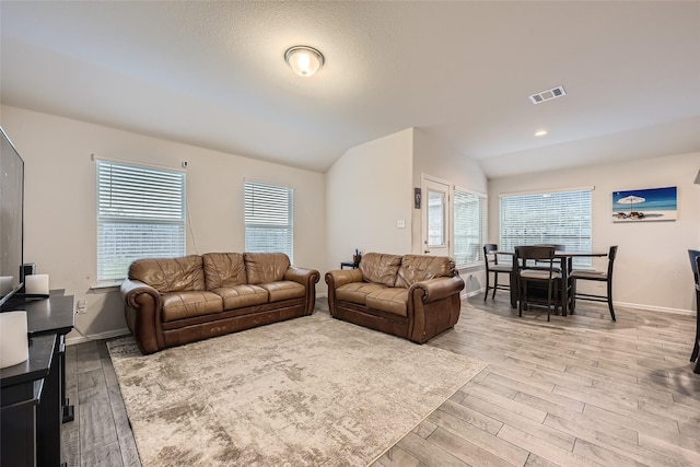 living room with baseboards, vaulted ceiling, light wood-type flooring, and visible vents