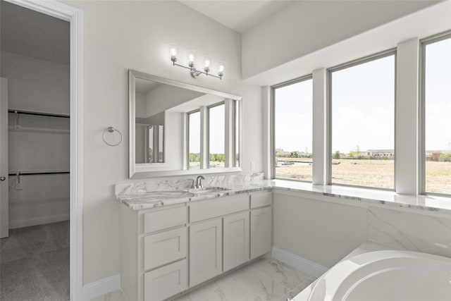 full bathroom featuring a tub, a walk in closet, baseboards, vanity, and marble finish floor