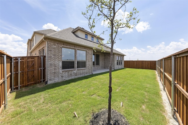 rear view of property featuring a lawn, brick siding, a fenced backyard, and roof with shingles