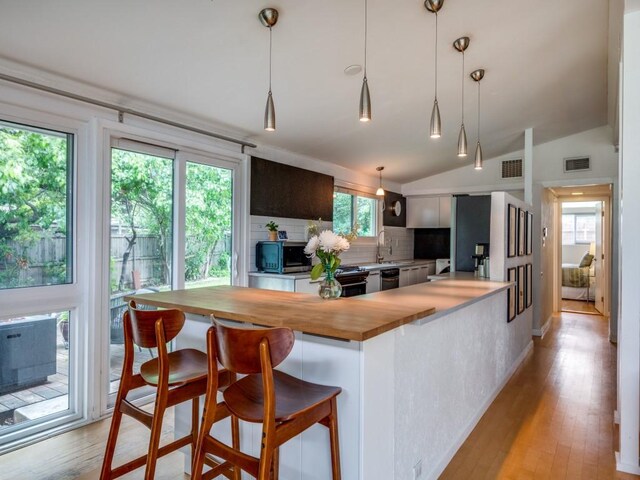 kitchen featuring vaulted ceiling, tasteful backsplash, wooden counters, and visible vents