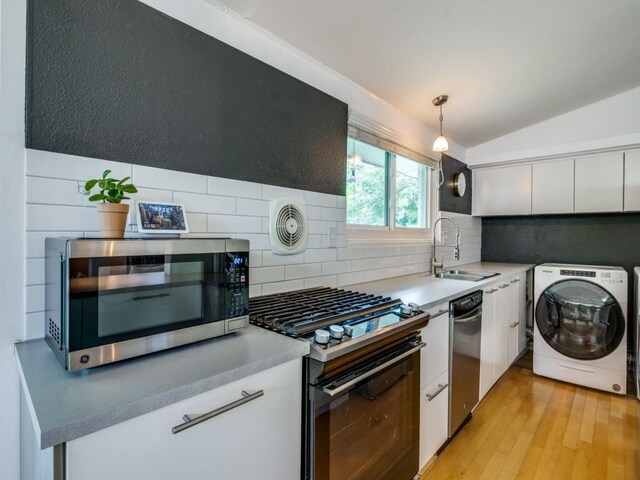 kitchen featuring washer / clothes dryer, vaulted ceiling, a sink, stainless steel appliances, and white cabinetry