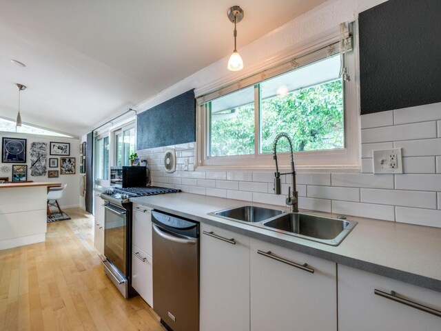 kitchen featuring pendant lighting, lofted ceiling, tasteful backsplash, a sink, and dishwasher