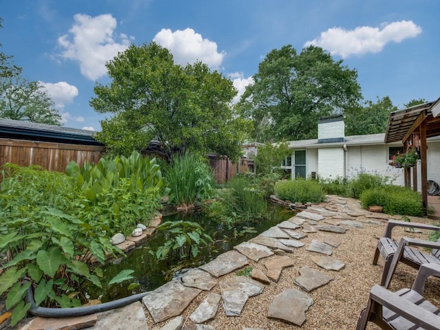 view of yard featuring fence and a garden pond