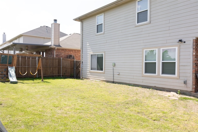 back of property featuring a playground, fence, and a yard