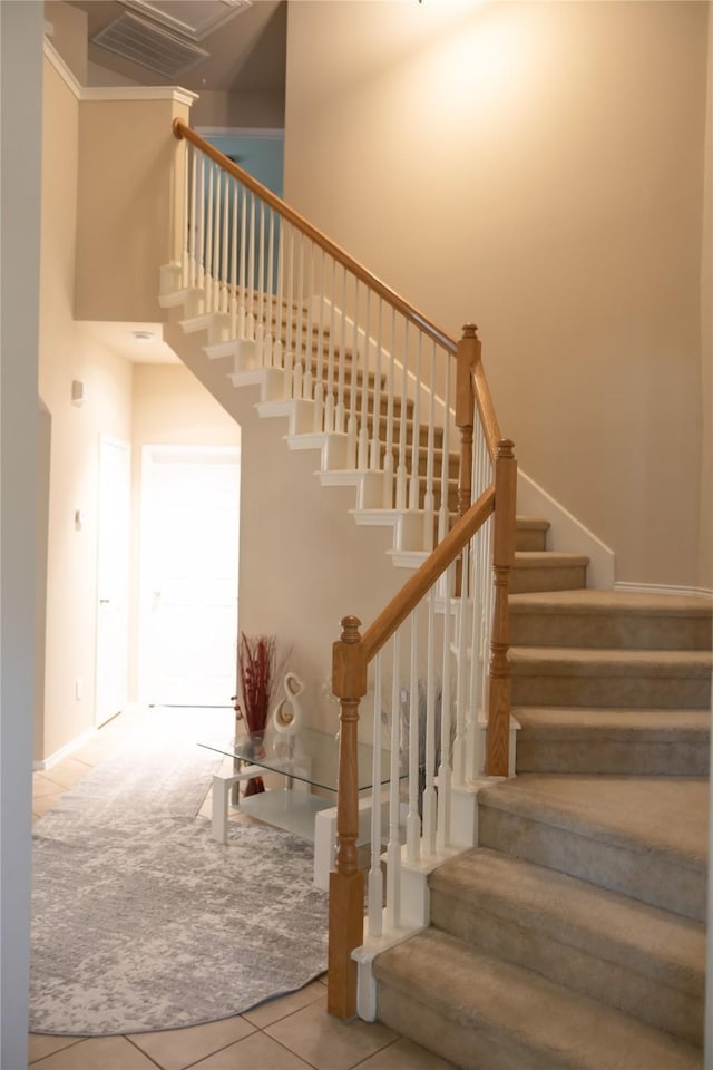 stairs featuring tile patterned flooring, baseboards, a towering ceiling, and visible vents