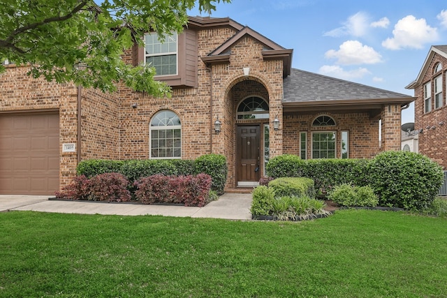 traditional-style house with a shingled roof, an attached garage, a front lawn, and brick siding