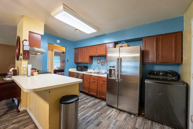 kitchen with a peninsula, wood finished floors, washer / clothes dryer, a sink, and appliances with stainless steel finishes