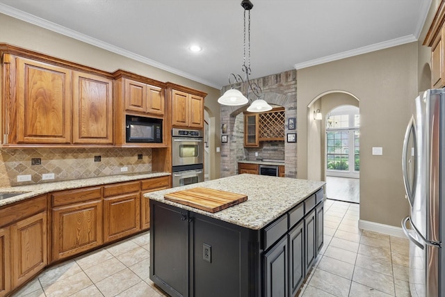 kitchen featuring backsplash, crown molding, arched walkways, brown cabinets, and stainless steel appliances