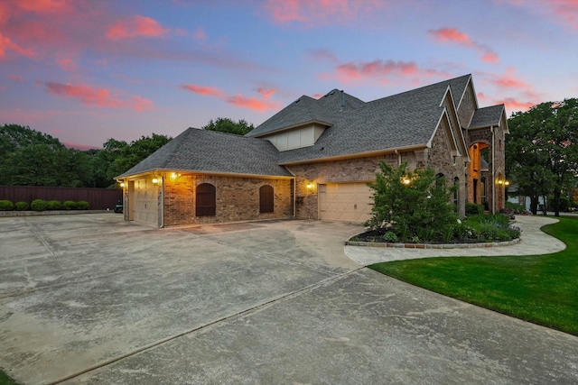 french provincial home featuring an attached garage, driveway, and roof with shingles