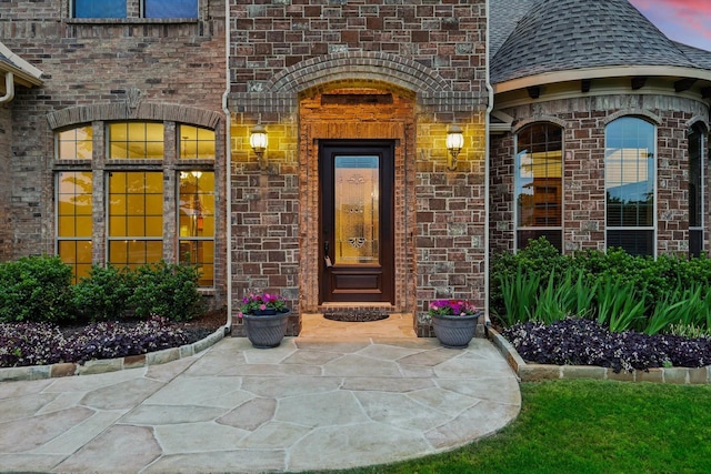 view of exterior entry with a shingled roof and brick siding