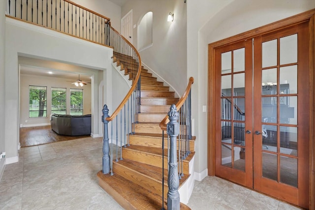 staircase with baseboards, ceiling fan, french doors, and a towering ceiling