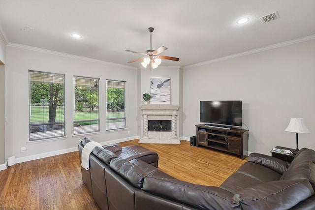 living room with ceiling fan, visible vents, wood finished floors, baseboards, and ornamental molding