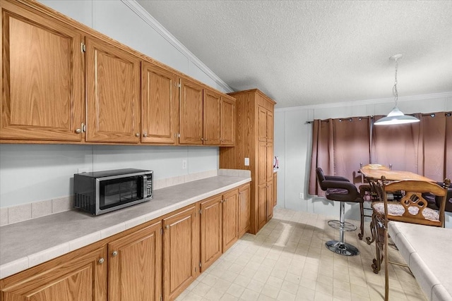 kitchen featuring crown molding, a textured ceiling, stainless steel microwave, and light countertops