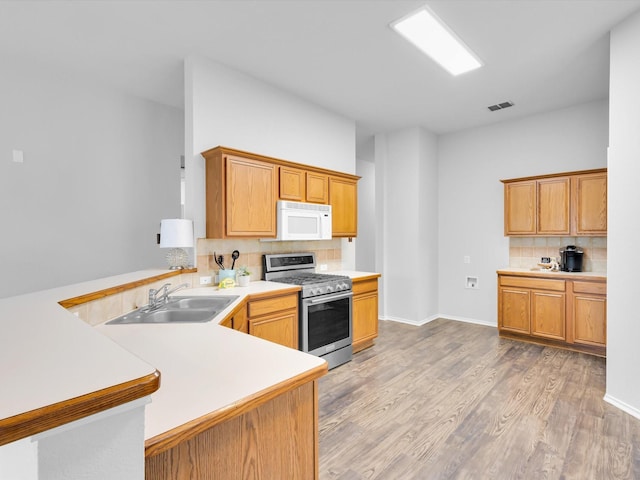 kitchen featuring a sink, stainless steel range with gas cooktop, a peninsula, white microwave, and visible vents