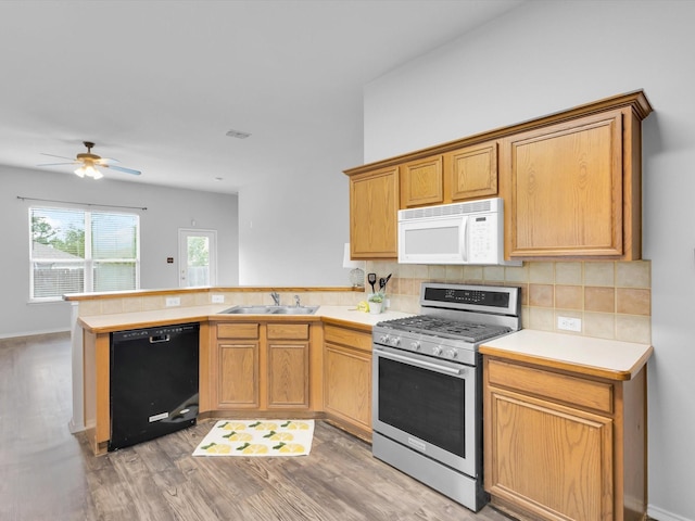 kitchen with a peninsula, white microwave, stainless steel range with gas cooktop, a sink, and dishwasher