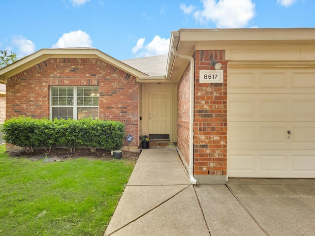 view of exterior entry with roof with shingles, brick siding, a garage, concrete driveway, and a lawn
