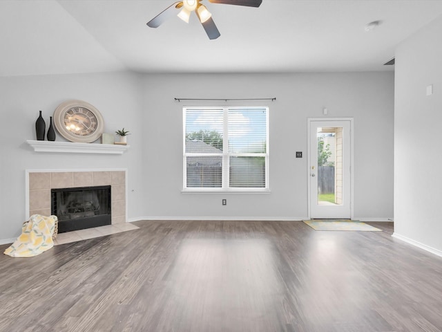 unfurnished living room with a ceiling fan, a tiled fireplace, a wealth of natural light, and wood finished floors