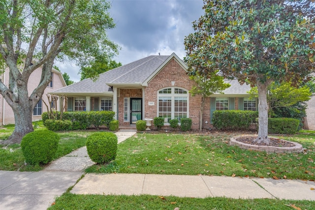 view of front facade featuring roof with shingles, brick siding, and a front yard