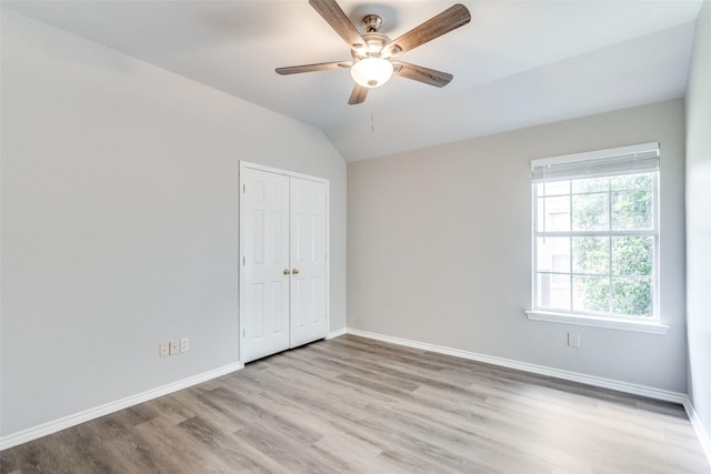 unfurnished bedroom featuring a closet, light wood-style floors, baseboards, a ceiling fan, and vaulted ceiling