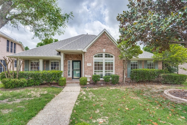 ranch-style home featuring brick siding, a shingled roof, and a front lawn