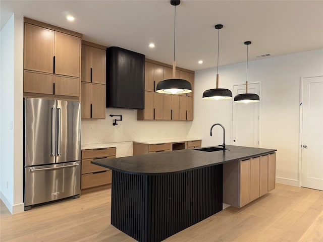 kitchen with dark countertops, light wood-style floors, high quality fridge, ventilation hood, and a sink