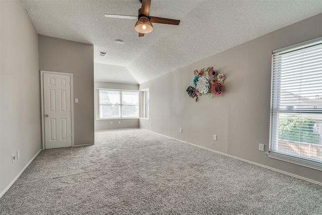 carpeted empty room with ceiling fan, a textured ceiling, visible vents, vaulted ceiling, and baseboards