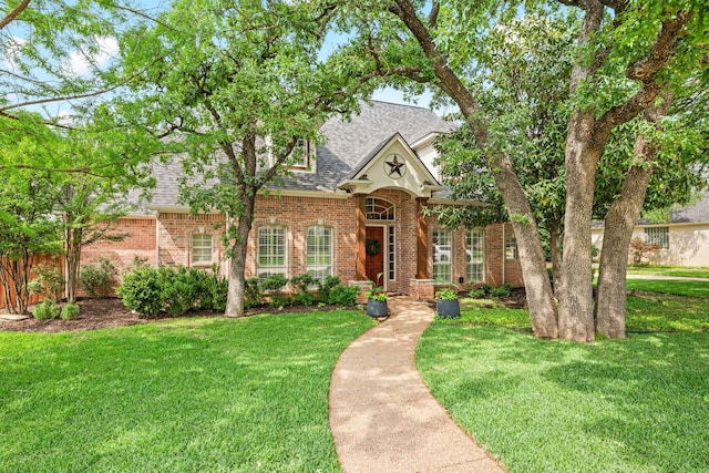 traditional-style house with a shingled roof, a front yard, and brick siding