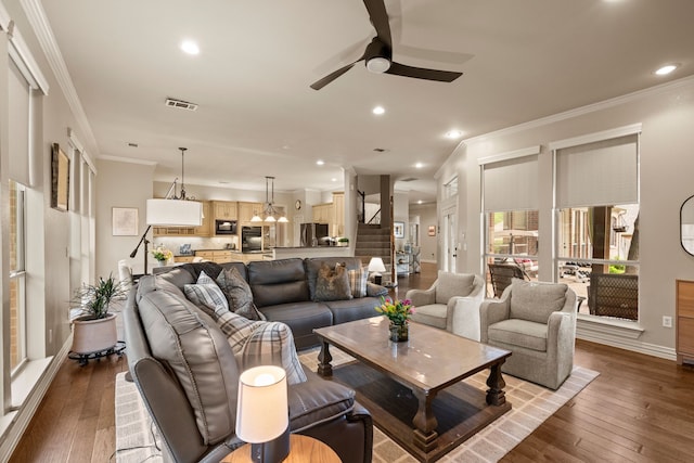 living room with wood-type flooring, a ceiling fan, visible vents, and ornamental molding