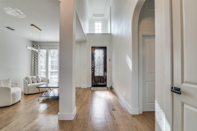 foyer featuring arched walkways, baseboards, visible vents, and light wood-type flooring