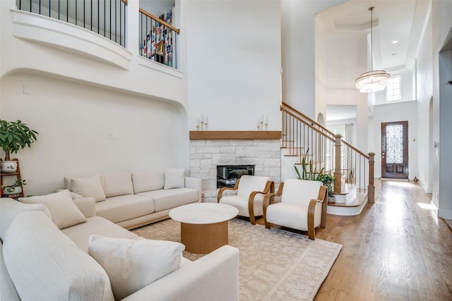 living room with an inviting chandelier, stairs, a towering ceiling, a stone fireplace, and light wood-type flooring