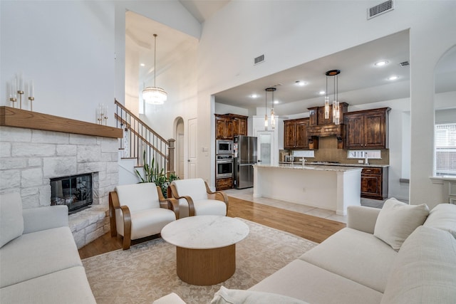 living area featuring arched walkways, visible vents, a stone fireplace, and light wood-type flooring