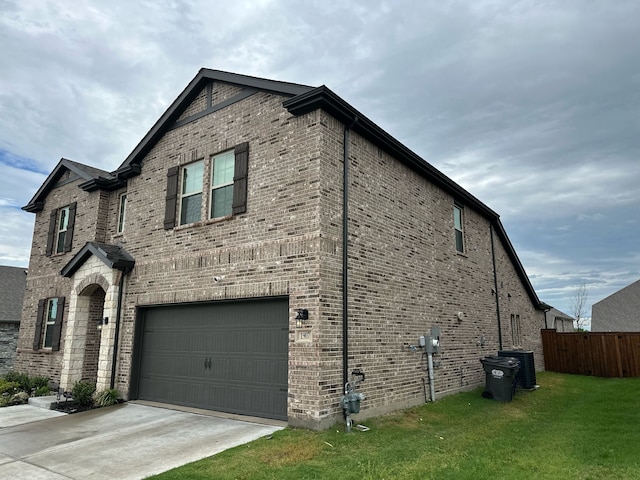 view of side of home featuring driveway, a garage, brick siding, fence, and a yard